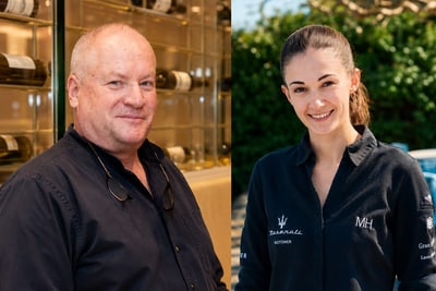 das-excellence-gourmetfestival-10.png Zwei Personen in dunkler Kleidung lächeln in die Kamera. Im Hintergrund sind Weinflaschen und draussen Sitzgelegenheiten zu sehen.