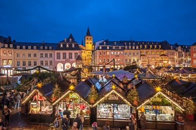 weihnachtsmarkt-in-trier.jpg Abendlicher Weihnachtsmarkt mit Lichtern und Ständen in einer historischen Stadt.
