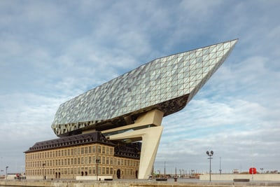 das-antwerpener-havenhuis-thront-wie-ein-riesiger-diamant-ue.jpg Modernes Gebäude mit glasüberdachtem Dach über historischem Backsteingebäude am Wasser.