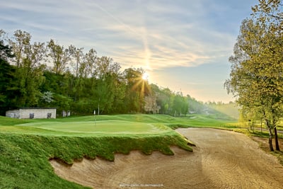 Sonnenaufgang über einem Golfplatz mit Bunker und Bäumen.