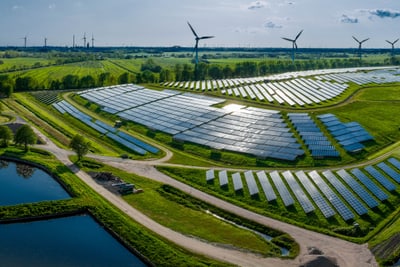 Luftaufnahme einer Solarfarm mit Windkraftanlagen und Teichen in einer grünen Landschaft.