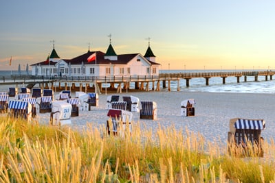 Strandkörbe am Sandstrand vor Seebrücke in der Abenddämmerung.