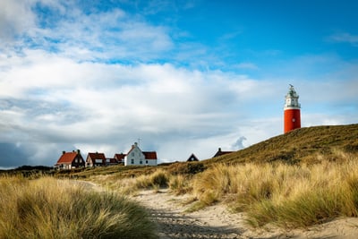 Roter Leuchtturm auf Düne mit Häusern im Hintergrund.
