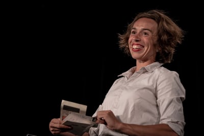 Person in einem weissen Hemd hält ein Buch und lächelt.