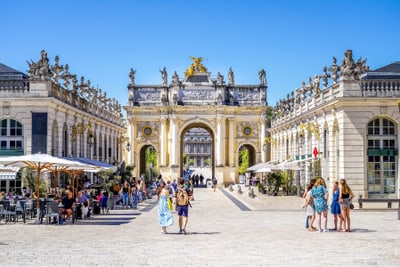 nancy-jugendstil-lebensart-und-genuss-im-herzen-lothringens.jpg Historischer Platz mit Torbogen, Skulpturen und Personen auf dem Kopfsteinpflaster.