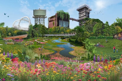 Üppige Gartenlandschaft mit Blumen, einem kleinen Fluss und industriellen Gebäuden im Hintergrund.