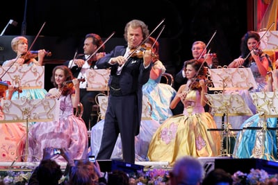 Geiger spielt mit Orchester auf Bühne in festlichen Kleidern.
