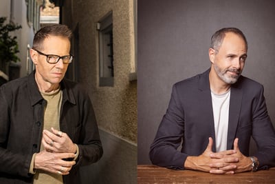 Zwei Männer; der eine in einer Gasse, der andere an einem Tisch sitzend.
