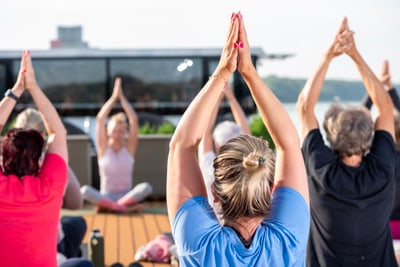 Gruppe von Menschen macht Yoga im Freien mit erhobenen Armen.