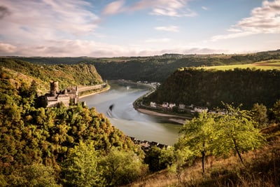 Burgruine am Fluss mit bewaldeten Hügeln im Hintergrund.