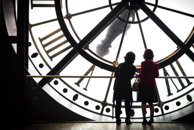 Zwei Personen vor grosser Uhr im Gebäudeinneren.