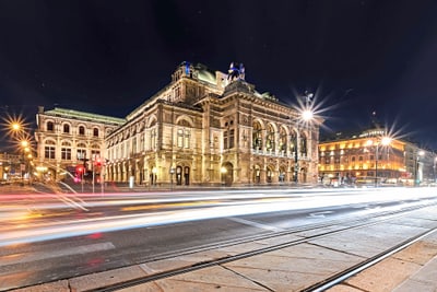 staatsoper-wien.jpg Beleuchtetes historisches Gebäude und bewegte Lichter von Autos bei Nacht.