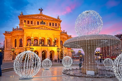 Beleuchtetes Opernhaus und Brunnen mit Lichterkugeln in der Abenddämmerung.
