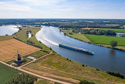 Luftaufnahme eines Flusses mit Schiff und Windmühle in der Landschaft.