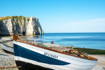 Strand mit Boot und Klippen im Hintergrund, klares blaues Meer.