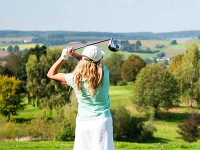 Frau schwingt Golfschläger auf grünem Golfplatz.