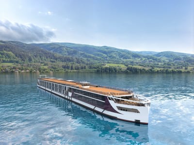 Flusskreuzfahrtschiff auf einem ruhigen Fluss vor bewaldeten Hügeln.