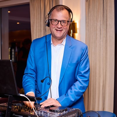 das-excellence-gourmetfestival-3.jpg Mann im blauen Anzug steht an einem DJ-Pult.