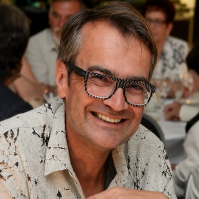 paris-die-normandie-und-das-meer-1.png Person mit Brille in weissem Hemd lächelnd bei einem formellen Essen.