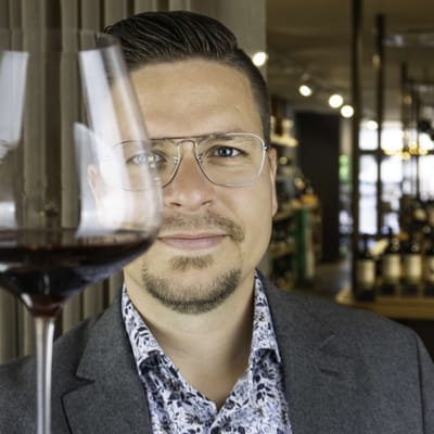 Mann mit Brille hält ein Glas Rotwein hoch.