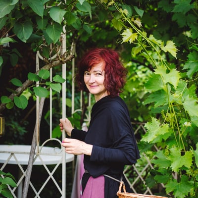 gartenparadiese-an-der-seine-1.jpg Person mit rotem Haar und Korb im Garten, umgeben von grünen Blättern.