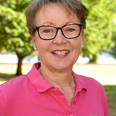 best-of-golf-donau-und-main-1.jpg Person mit Brille in einem pinken Oberteil vor einem Baum im Freien.