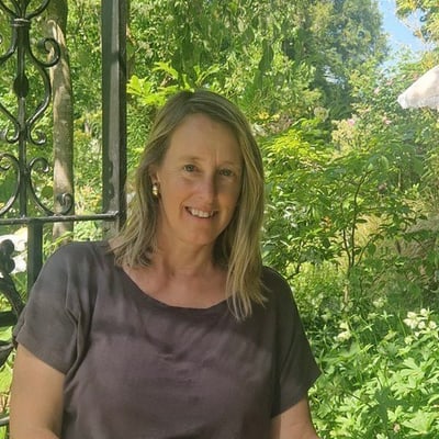 Person in grauem Oberteil im Garten sitzend.