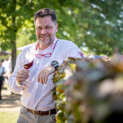 weinexperte-geny-hess.jpg Mann im Freien mit Weinglas lächelt in die Kamera.