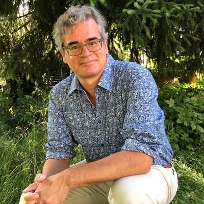 urs-heinz-aerni-fachbegleitung-der-reise.jpg Mann in gemustertem Hemd sitzt im Garten.