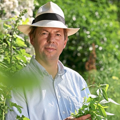 Mann mit Hut in einem Garten stehend.