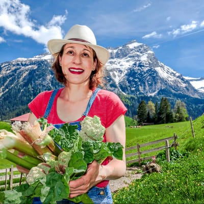 suedfrankreichs-gruene-oasen-1.jpg Person in rotem T-Shirt mit Hut hält Gemüse in einer Berglandschaft.