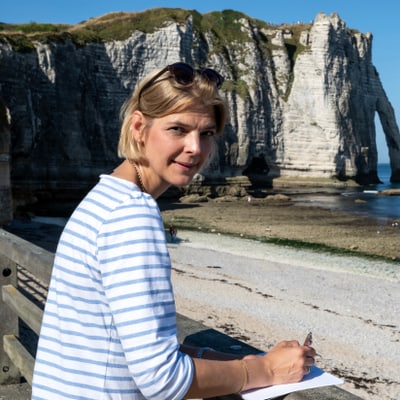 die-seine-und-ihre-impressionisten-1.jpg Frau am Strand mit Notizblock, Klippe im Hintergrund.