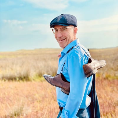 franken-und-die-oberpfalz-sommertage-zum-geniessen-1.jpg Person im blauen Hemd und Mütze steht auf einem Feld mit trockenen Gräsern.