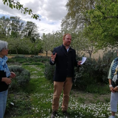 Menschengruppe in einem Garten mit Bäumen und Blumen.