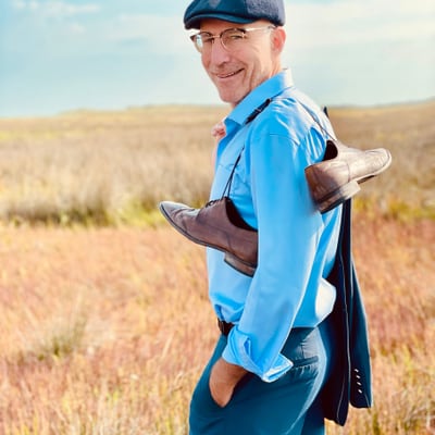 franken-und-die-oberpfalz-sommertage-zum-geniessen-1.jpg Person im blauen Hemd und Mütze steht auf einem Feld mit trockenen Gräsern.