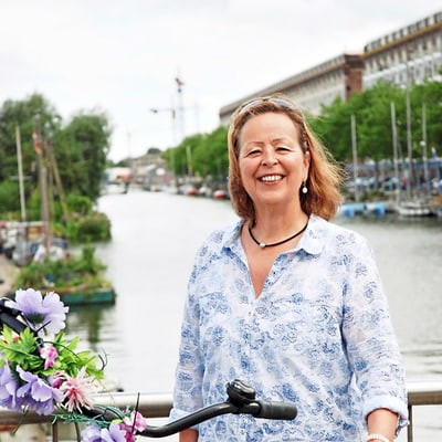 grand-tour-nordische-sommer-cruise-1.jpg Frau mit Fahrrad auf einer Brücke vor einem Fluss.