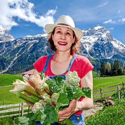 lavendelbluete-in-der-provence-1.jpg Frau mit Hut hält Gemüse vor Berglandschaft.