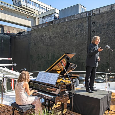 excellence-exklusiv-aus-purer-liebe-zur-musik-1.jpg Frau am Klavier und Mann am Mikrofon auf Boot vor Schleuse.