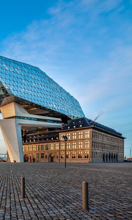 Das Havenhuis in Antwerpen: moderner Glasaufbau von Zaha Hadid über historischer Feuerwache am Hafenbecken.