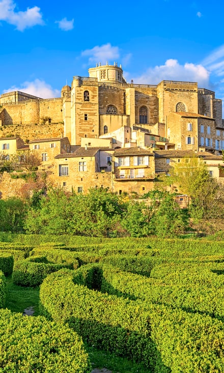 Geometrisch angelegter Heckengarten in Grignan mit historischer Altstadt auf dem Hügel dahinter.