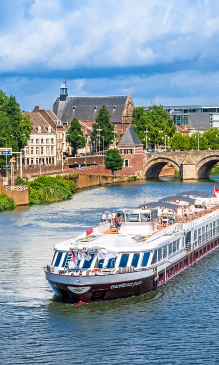 excellence-pearl.jpg Flusskreuzfahrtschiff auf einem Fluss mit Brücke und Altstadt im Hintergrund.