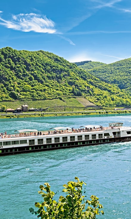 excellence-pearl.jpg Flusskreuzfahrtschiff auf dem Rhein von grünen Hügeln umgeben.