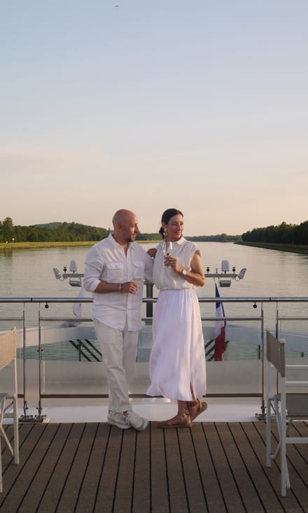 white-night-an-bord-der-excellence-crown.jpg Zwei Personen auf einem Boot, umgeben von Wasser und Stühlen, bei Sonnenuntergang.