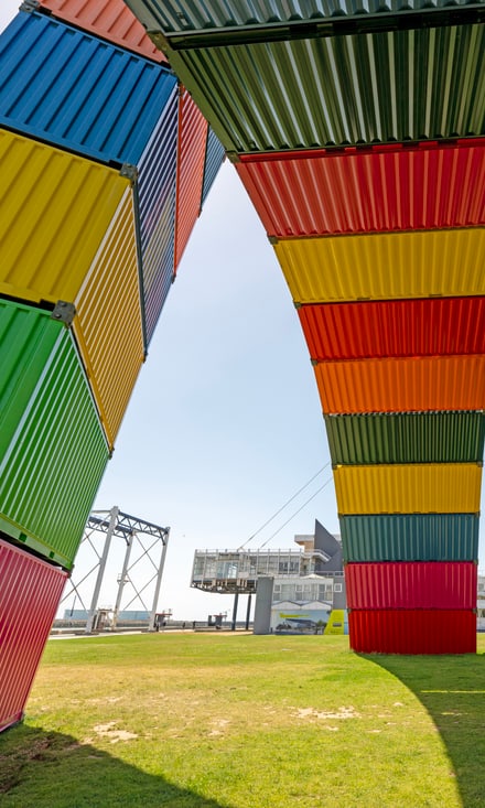 Bogenförmige Skulptur aus bunten Schiffscontainern in Le Havre, Frankreich, vor blauem Himmel.