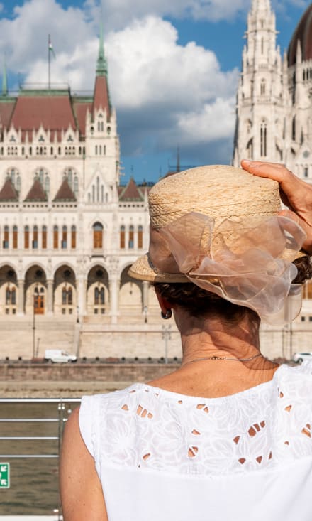 Person mit Strohhut betrachtet historisches Gebäude am Flussufer.
