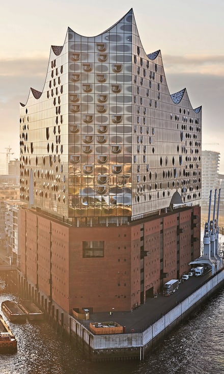 Luftaufnahme der Elbphilharmonie Hamburg mit Glaswellendach über Backsteinbau, Fluss und Brücke im Abendlicht.