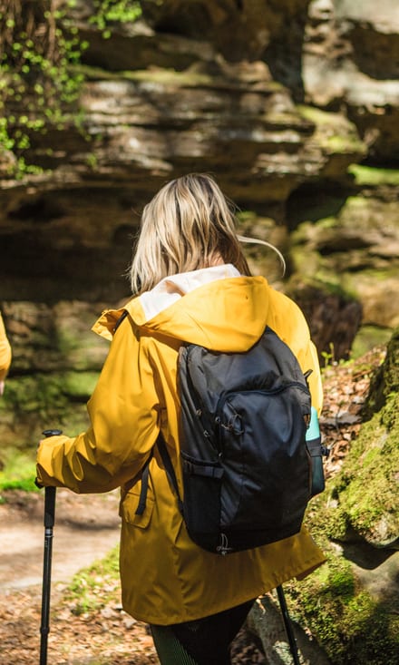 Mann und Frau mit Rucksäcken und Wanderstöcken wandern durch moosbedeckte Felsen im Wald.