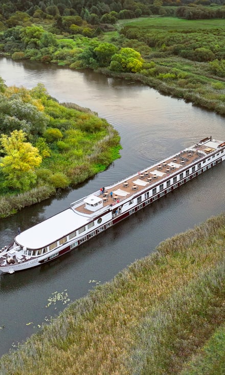 Das Flussschiff Excellence Coral gleitet auf der Peene bei Demmin durch üppige Flusslandschaft, aufgenommen aus der Luft.