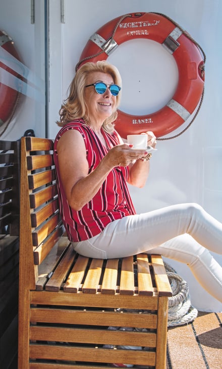 Frau mit Kaffeetasse sitzt auf dem Sonnendeck der Excellence Coral und blickt auf den Fluss.