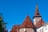 Gebäude mit gemusterten Dächern und Turm vor blauem Himmel.